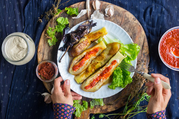 Woman hands cut roasted  grilled eggplants with fork and knife dressed with tomato garlic sauce, paprika, pepper and fresh salad leaves for lunch or dinner. Raw vegan vegetarian healthy food.