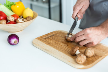 Poster - close-up partial view of man cutting fresh mushrooms on wooden cutting board