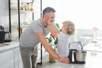 Wall Mural - side view of little boy touching smiling father cheeks near tabletop at kitchen