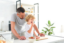 Smiling Father Standing Near Son While He Eating Strawberry At Kitchen