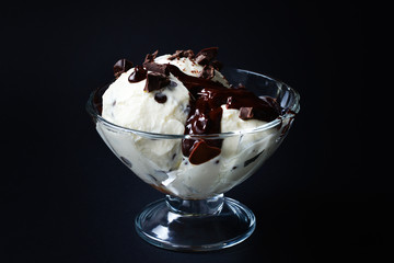 Vanilla ice cream in a white bowl with chocolate on a black background.