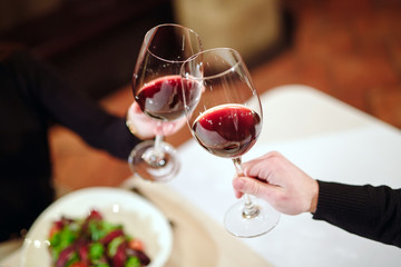 Man and woman drinking red wine. In the picture, close-up hands with glasses.