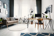 Workspace hairpin desk with mockup computer, lamp and decor standing in living room interior with posters on texture wall, round carpet, sofa with pillows and bike under windows