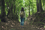 Fototapeta Nowy Jork - Young woman with backpack explores map on forest path. Woman with tourist backpack travels