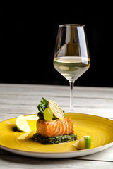 The concept of a beautiful european dish in the restaurant. steak fillet of red salmon fish or trout on spinach cushions, next to a glass of white wine on the table