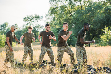 Wall Mural - side view of interracial soldiers practicing with tires on ground on range