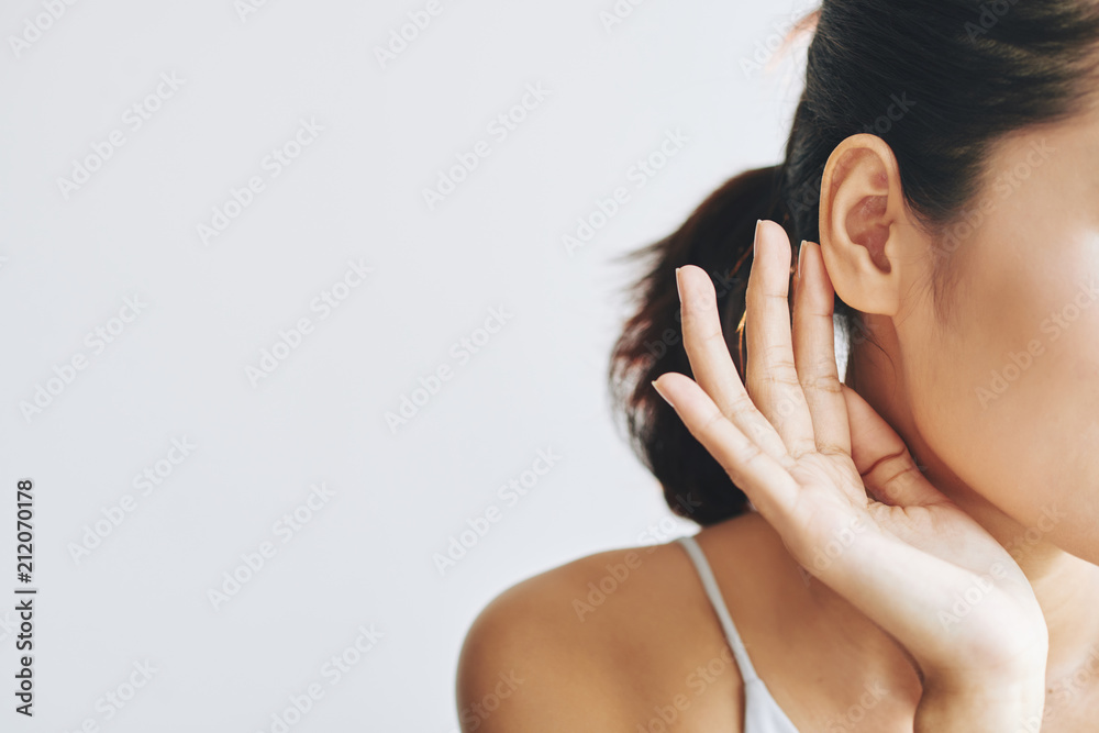 Crop female with dark hair in ponytail touching ear with help of fingers and with tenderness on grey background - obrazy, fototapety, plakaty 