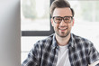 portrait of handsome young man in eyeglasses smiling at camera at workplace