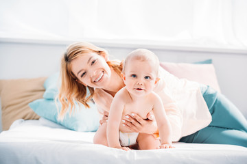 Wall Mural - mother supporting her little child while he crawling on bed at home