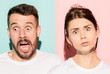 © master1305 - Closeup portrait of young couple, man, woman. One being excited happy smiling, other serious, concerned, unhappy on pink and blue background. Emotion contrasts