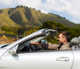 Fototapeta Tulipany - road trip, travel and people concept - happy man driving convertible car over big sur hills background in california