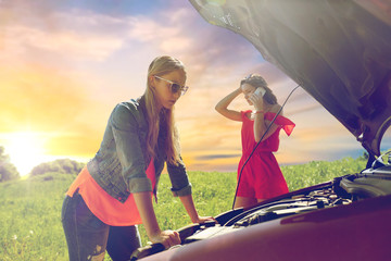 Wall Mural - road trip, transport, travel and people concept - young women with open hood of broken car at countryside calling on smartphone to evacuation service over evening sky background