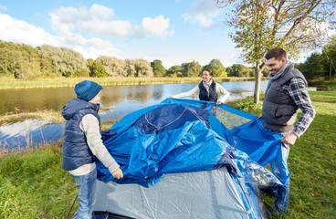 Wall Mural - camping, tourism and family concept - happy mother, father and son setting up tent at campsite