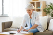 © Syda Productions - business, savings, annuity insurance, age and people concept - senior woman with papers or bills and calculator writing at home