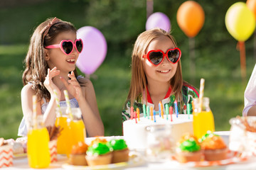 holidays, childhood and celebration concept - happy kids with candles on birthday cake sitting at table at summer garden party