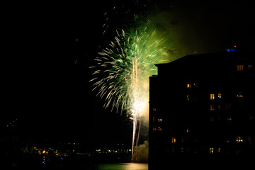 A Fourth of July fireworks display explodes over the waterfront in the city center of Norfolk Virginia, in the context of buildings, apartments, and dwellings