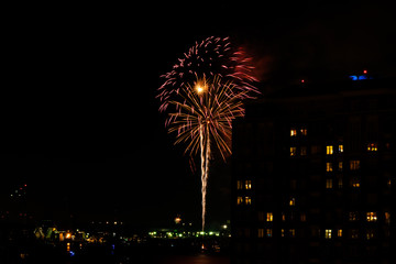 A Fourth of July fireworks display explodes over the waterfront in the city center of Norfolk Virginia, in the context of buildings, apartments, and dwellings