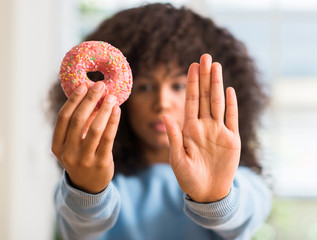 Poster - African american woman holding donut at home with open hand doing stop sign with serious and confident expression, defense gesture