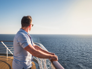 Attractive man in sunglasses on the top deck of a cruise ship looking out into the distance against the background of a sunset. Concept of sea travel and recreation