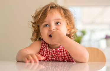 Beautiful blonde child with blue eyes smiling and eating candy at home.