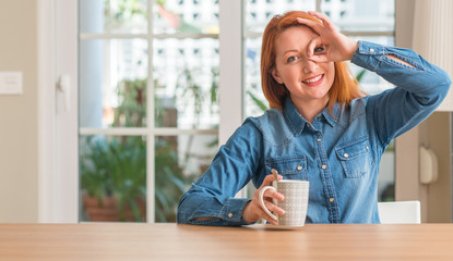 Sticker - Redhead woman holding a cup of coffee with happy face smiling doing ok sign with hand on eye looking through fingers