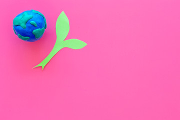 Wall Mural - Planet, ecology. plastiline symbol of planet Earth globe and plant coutout on pink background top view copy space