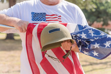 American Veteran Proudly Holding Military WWI Helmet (M1 Helmet) And US Flag During Parade. July 4th Or Veteran Memorial Day Poster Of WWII, Modern Wars. Honor And Remember Soldier Troop Background