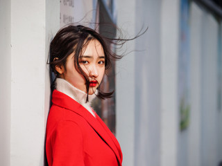 Beautiful young brunette woman wearing a red coat in autumn city. Outdoor fashion portrait of glamour young Chinese cheerful stylish lady in street. Emotions, people, beauty and lifestyle concept.