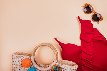 Wall Mural - Summer fashion flatlay with brown sunglasses, trendy straw bag with pompoms and red swimsuit with frills on the beige background. Perfect beach set for holidays on the sea. Marina style.