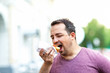 Portrait of bearded caucasian man eating hot dog at street background.