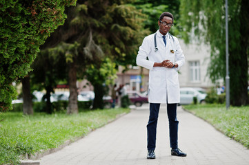 Wall Mural - Stylish african american doctor with stethoscope and lab coat, at glasses posed outdoor.