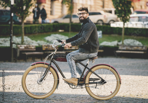 Fotografie, Obraz Bearded Smiling Young Man in Glasses Riding Bike.