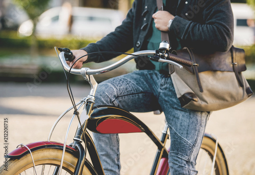 Fotografie, Obraz Young Man in Jeans Pants with Bag Riding Bike.