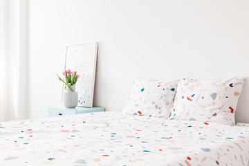 Wall Mural - Flowers and poster on cabinet next to patterned bed in bright modern bedroom interior. Real photo