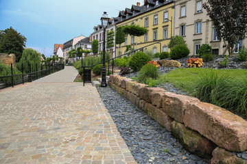 Canvas Print - Moderner Garten und Landschaftsbau: Mauer aus Natursteinen und Weg aus Natur Pflastersteinen an der Promenade entlang des Flusses Lauch in Colmar, Elsass