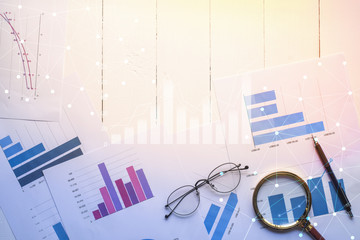 Magnifying glass and documents with analytics data lying on table,selective focus