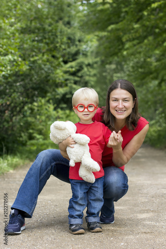 Fotografia, Obraz Mother and her cute toddler son with plush bear and toy glasses outdoor