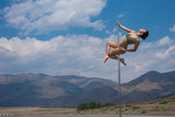 woman dancing on a pole among the mountains. young girl pole dancing out of doors