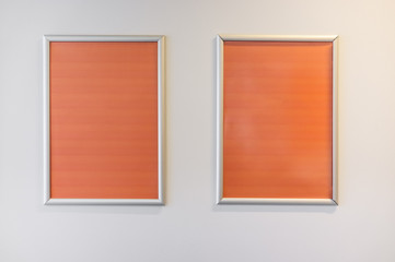 Two picture frames with orange copy space hanging on white wall