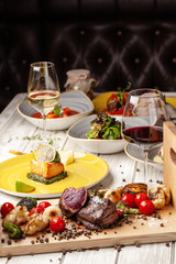 Two juicy steaks with roast medium rare, with grilled vegetables on a wooden board. Cooked with air fryers. A laid table in the restaurant for a holiday or birthday, evening dinner. selective focus