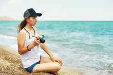 Attractive Girl With A Camera On The Sea Coast . Young Stylish Woman Photographer On A Walk By The Sea