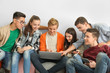 © Africa Studio - Group of teenagers with modern devices sitting near white wall