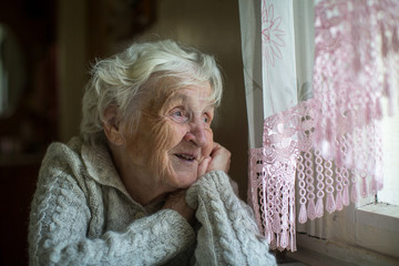 Wall Mural - A gray-haired elderly woman sits and looks out the window.