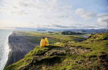 Wall Mural - a young boy and girl sit on a cliff and hug. iceland. vik