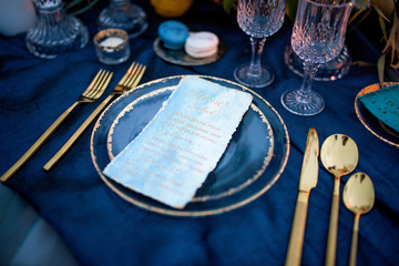 Wall Mural - Menu card lies on a blue plate surrounded with golden dinner set