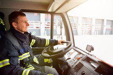 Smiling Fireman At The Wheel Of A Fire Truck Drives To Work