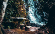 Magical Dark Forsaken Place In The Rainforest With Ancient Stone Table And Backless Stools Near It, Waterfall In A Defocused Background; Shallow Depth Of Field, The Jungle Of Ibitipoca, Brazil