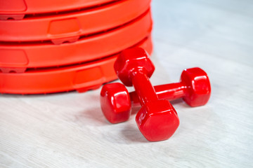 Red modern dumbbells and pancakes for dumbbells in the foreground on a wooden floor