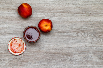 Open glass with nectarine jam beside two fresh fruits isolated on wooden table