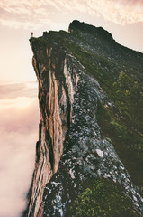 Man standing on cliff edge mountain ridge above sunset clouds travel adventure lifestyle summer journey vacations